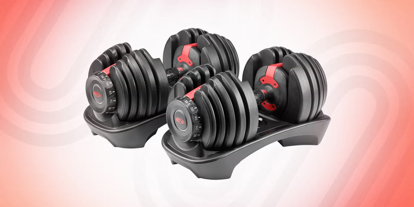 Pair of black and red Boulders & Shoulders adjustable dumbbells in storage trays on a light wood home gym floor, showing weight adjustments from 5 to 52.5 lbs.